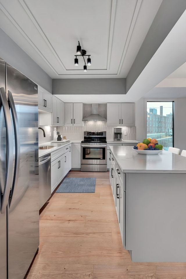 kitchen featuring light wood-type flooring, sink, wall chimney exhaust hood, stainless steel appliances, and decorative backsplash