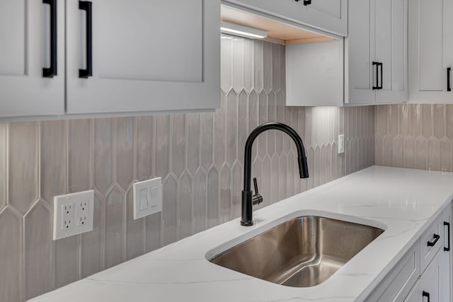 interior details with light stone counters, sink, and white cabinetry