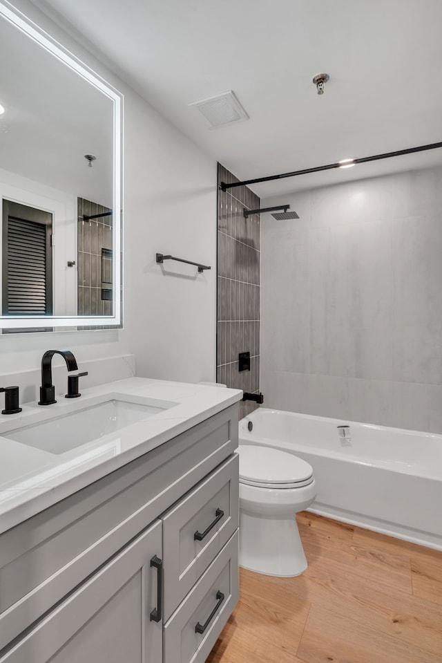 full bathroom with hardwood / wood-style floors, vanity, toilet, and tiled shower / bath