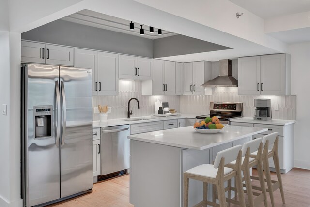 kitchen with sink, a kitchen island, light hardwood / wood-style flooring, wall chimney exhaust hood, and appliances with stainless steel finishes