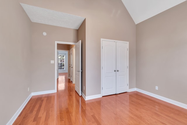 unfurnished bedroom with a textured ceiling, vaulted ceiling, a closet, and hardwood / wood-style flooring