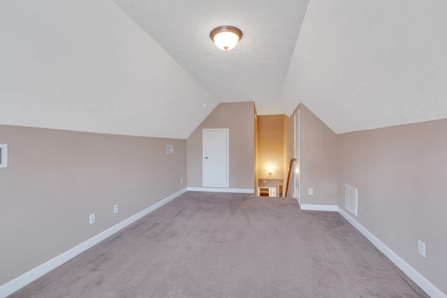 bonus room with light carpet, lofted ceiling, and a textured ceiling