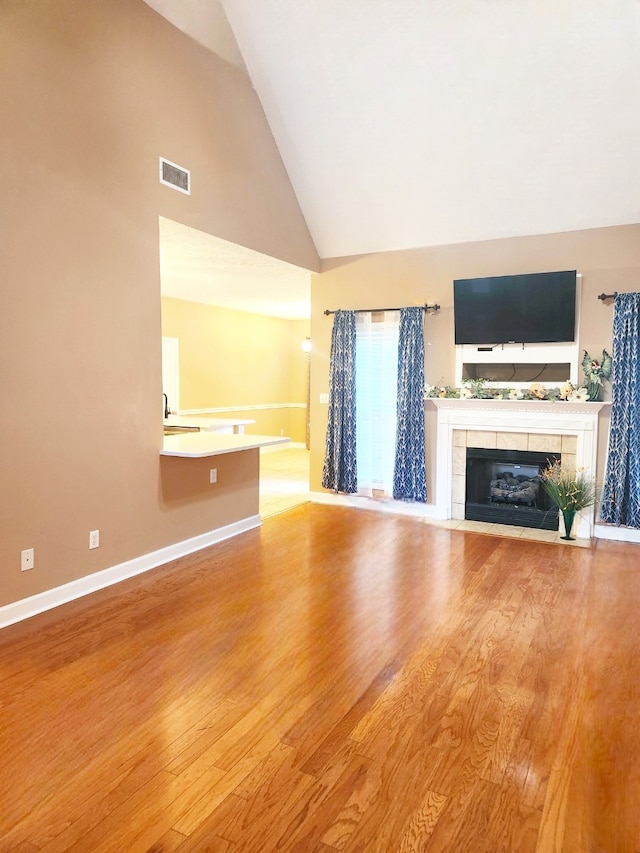 unfurnished living room featuring hardwood / wood-style flooring, high vaulted ceiling, and a tile fireplace