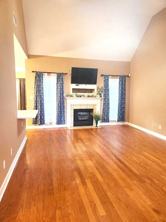 unfurnished living room with a tile fireplace, lofted ceiling, hardwood / wood-style floors, and a wealth of natural light