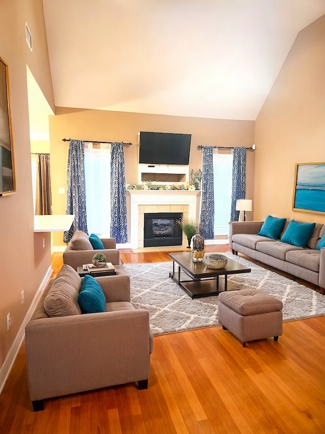 living room featuring high vaulted ceiling, a fireplace, hardwood / wood-style flooring, and a healthy amount of sunlight