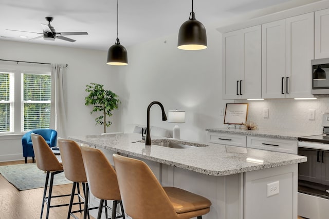 kitchen featuring white cabinets, stainless steel appliances, ceiling fan, a kitchen island with sink, and sink