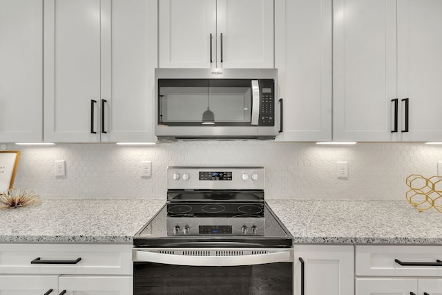 kitchen featuring white cabinets, stainless steel appliances, light stone countertops, and decorative backsplash