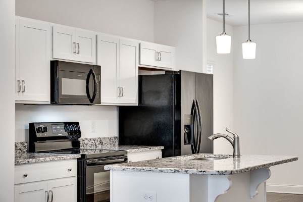 kitchen featuring black appliances, white cabinetry, light stone countertops, and decorative light fixtures