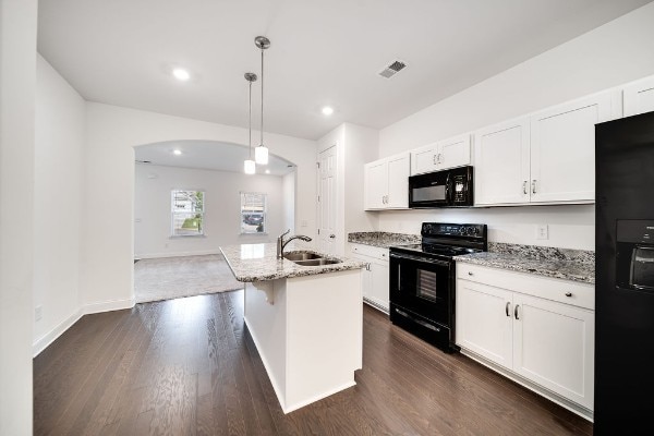 kitchen featuring dark wood-type flooring, white cabinets, black appliances, a center island with sink, and decorative light fixtures