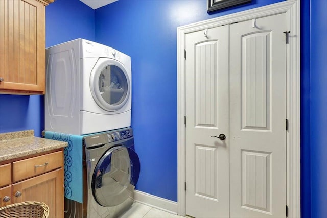 laundry room featuring cabinets, stacked washer / dryer, and light tile patterned floors