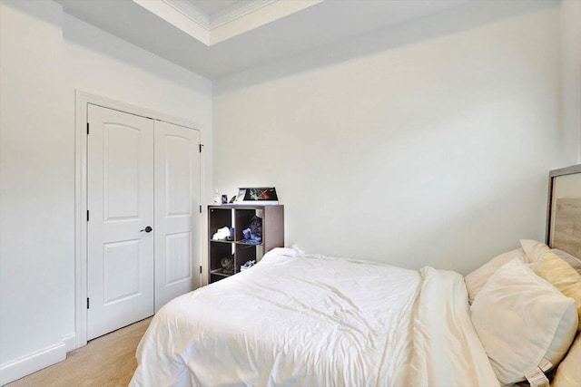 bedroom with a closet, crown molding, a tray ceiling, and light colored carpet
