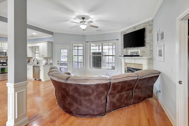 living room with light wood-type flooring, crown molding, a large fireplace, and ceiling fan