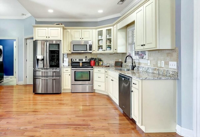 kitchen featuring ornamental molding, a sink, light wood-style flooring, light stone countertops, and appliances with stainless steel finishes