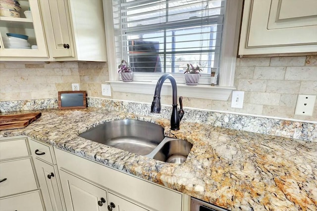 kitchen featuring a sink, tasteful backsplash, light stone counters, and glass insert cabinets