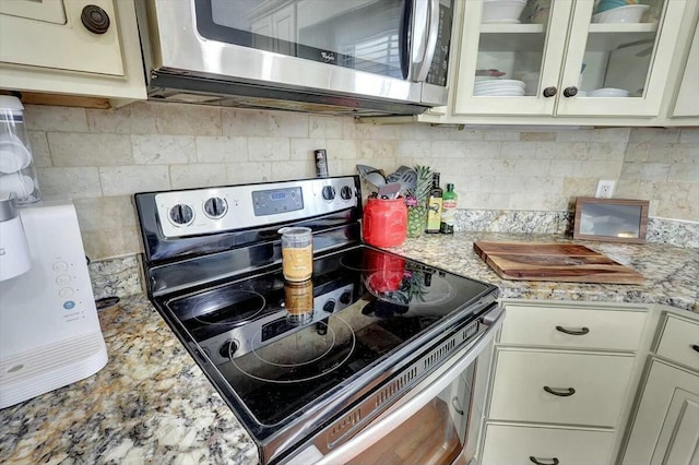 kitchen with light stone counters, white cabinetry, tasteful backsplash, glass insert cabinets, and stainless steel appliances