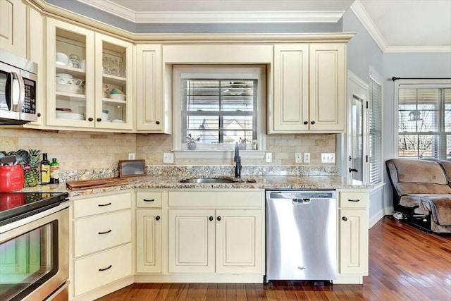 kitchen with cream cabinetry, a sink, appliances with stainless steel finishes, and crown molding