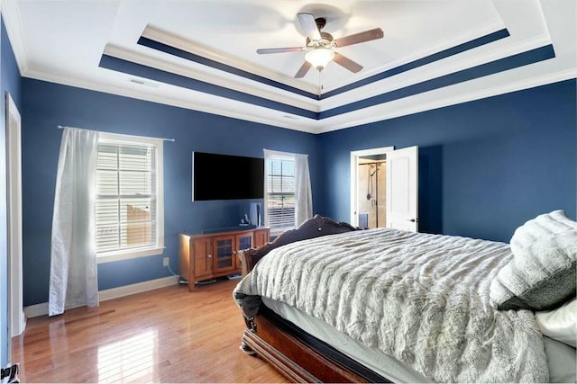bedroom with light wood-type flooring, ornamental molding, baseboards, a raised ceiling, and visible vents