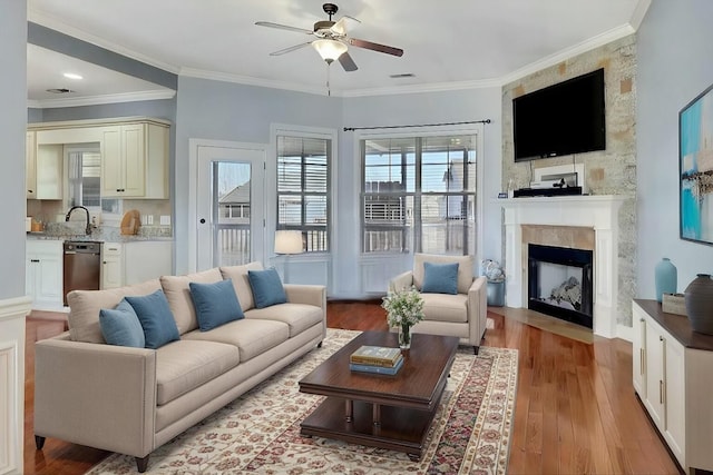 living area with a fireplace with flush hearth, visible vents, crown molding, light wood finished floors, and a ceiling fan
