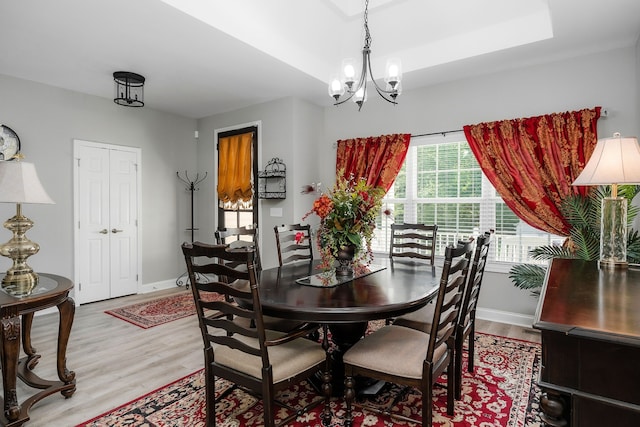 dining area with light hardwood / wood-style flooring, a tray ceiling, and a notable chandelier