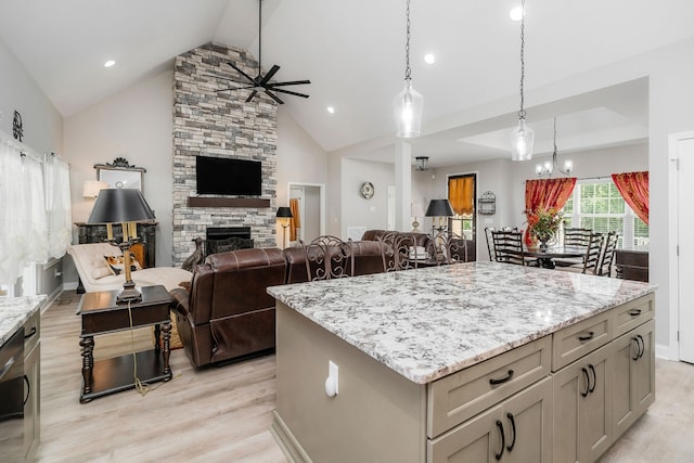 kitchen featuring pendant lighting, a fireplace, a center island, ceiling fan with notable chandelier, and light hardwood / wood-style floors