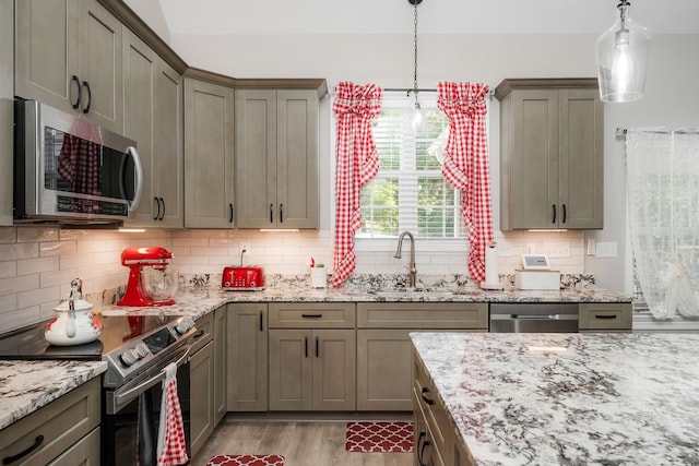 kitchen featuring decorative backsplash, light stone counters, stainless steel appliances, decorative light fixtures, and sink