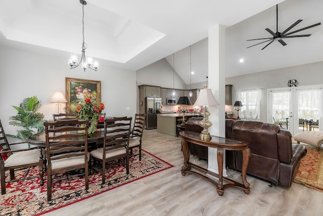 dining area with ceiling fan with notable chandelier, light hardwood / wood-style floors, and high vaulted ceiling