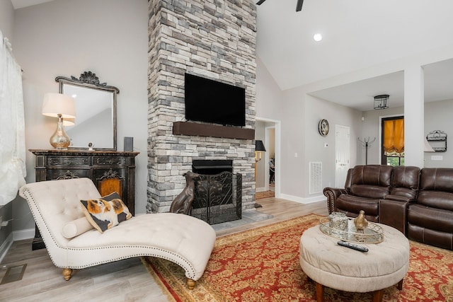 living room featuring light hardwood / wood-style flooring, high vaulted ceiling, and a stone fireplace