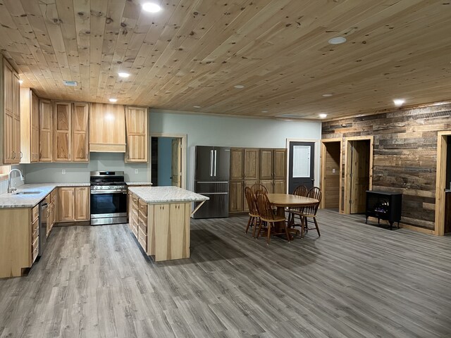 kitchen with custom range hood, light hardwood / wood-style floors, a kitchen island, stainless steel appliances, and wooden walls