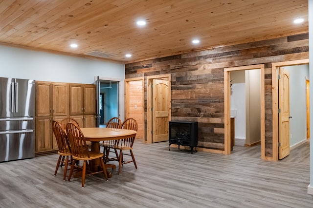 dining area featuring wooden ceiling, light hardwood / wood-style floors, wooden walls, and a wood stove