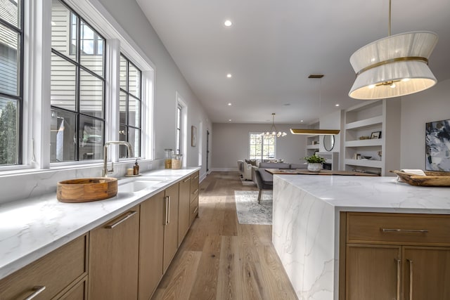 kitchen featuring built in shelves, light stone countertops, sink, decorative light fixtures, and light wood-type flooring