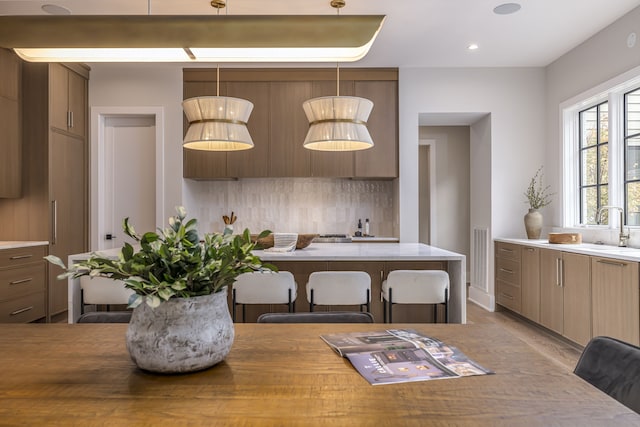 kitchen with backsplash, sink, pendant lighting, and light hardwood / wood-style flooring