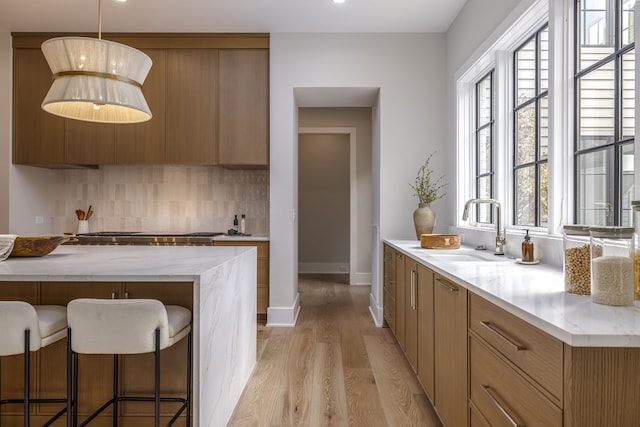 kitchen with sink, tasteful backsplash, light hardwood / wood-style flooring, decorative light fixtures, and a breakfast bar area