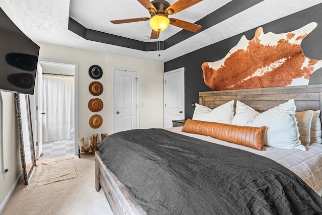 bedroom featuring ceiling fan, light colored carpet, a textured ceiling, and a tray ceiling