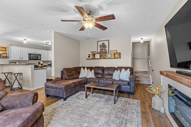 living room with a textured ceiling, wood-type flooring, and ceiling fan