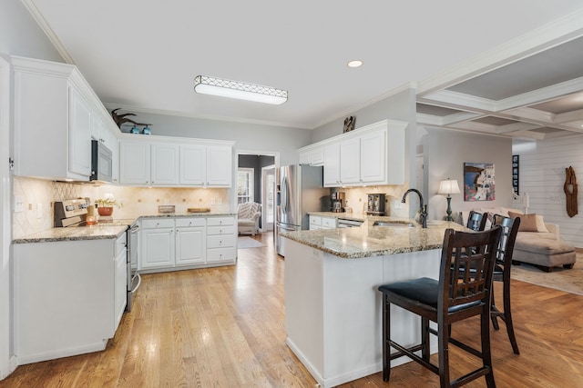 kitchen featuring appliances with stainless steel finishes, white cabinets, kitchen peninsula, light wood-type flooring, and sink