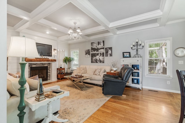 living room featuring beam ceiling, wood-type flooring, a stone fireplace, coffered ceiling, and a notable chandelier