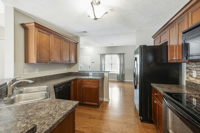 kitchen with a textured ceiling, black appliances, dark hardwood / wood-style flooring, and sink