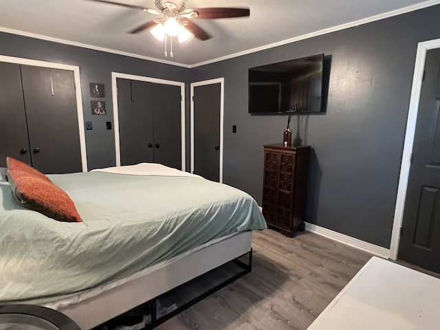 bedroom featuring ceiling fan, hardwood / wood-style floors, two closets, and ornamental molding