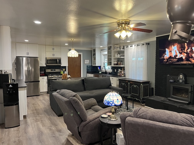 living room featuring light wood-type flooring, ceiling fan, ornamental molding, and sink