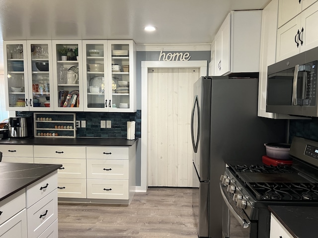 kitchen with white cabinets, dark stone countertops, stainless steel appliances, and light hardwood / wood-style flooring