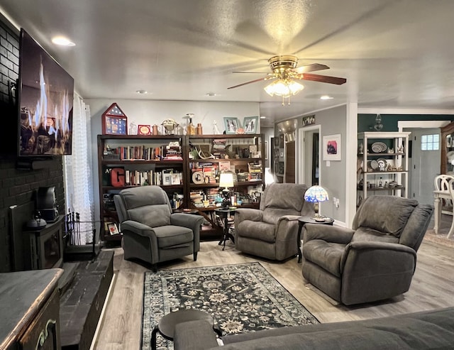 living room with light hardwood / wood-style floors, a wood stove, and ceiling fan