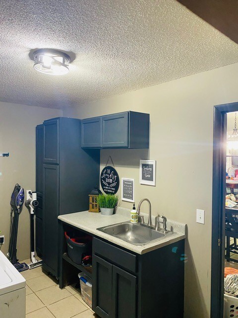 kitchen featuring blue cabinets, light tile patterned floors, a textured ceiling, and sink