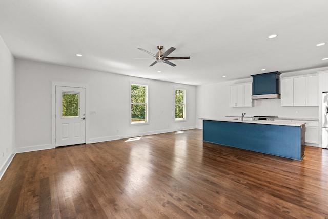 kitchen with ceiling fan, white cabinets, custom exhaust hood, a kitchen island with sink, and dark hardwood / wood-style flooring