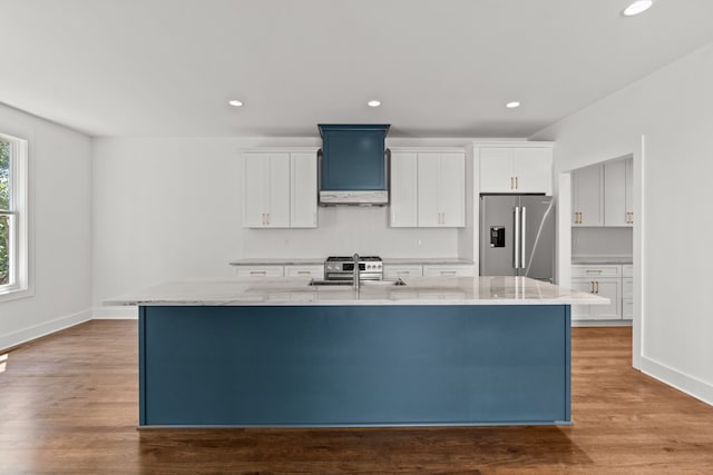 kitchen featuring appliances with stainless steel finishes, custom exhaust hood, an island with sink, and white cabinets