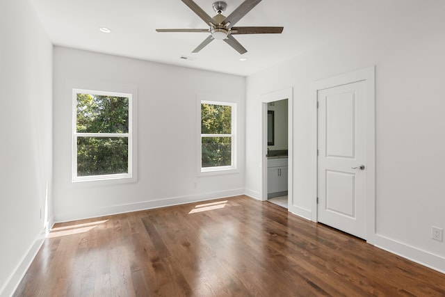 unfurnished bedroom with connected bathroom, multiple windows, ceiling fan, and dark hardwood / wood-style flooring