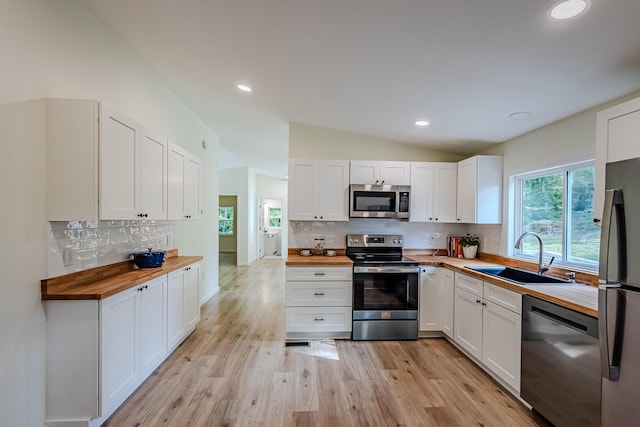 kitchen featuring white cabinets, lofted ceiling, sink, appliances with stainless steel finishes, and wood counters