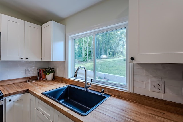 kitchen with butcher block countertops, sink, decorative backsplash, and white cabinetry