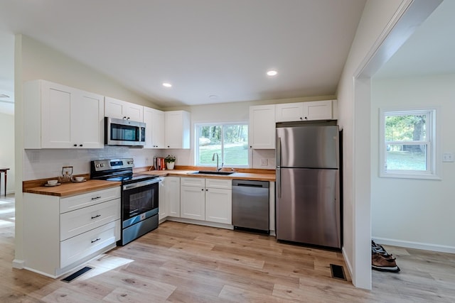 kitchen with appliances with stainless steel finishes, white cabinetry, wooden counters, light wood-type flooring, and sink