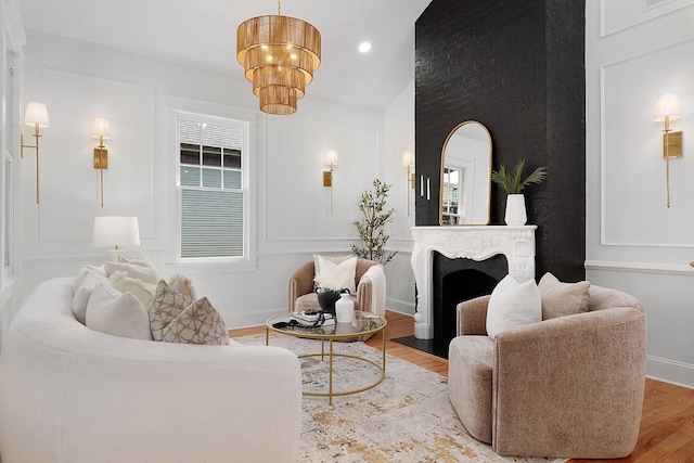 living room with a fireplace, a chandelier, vaulted ceiling, and light hardwood / wood-style flooring