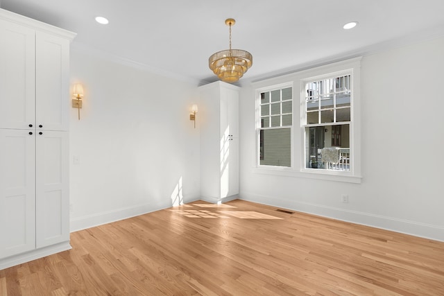 spare room featuring light hardwood / wood-style floors, an inviting chandelier, and ornamental molding